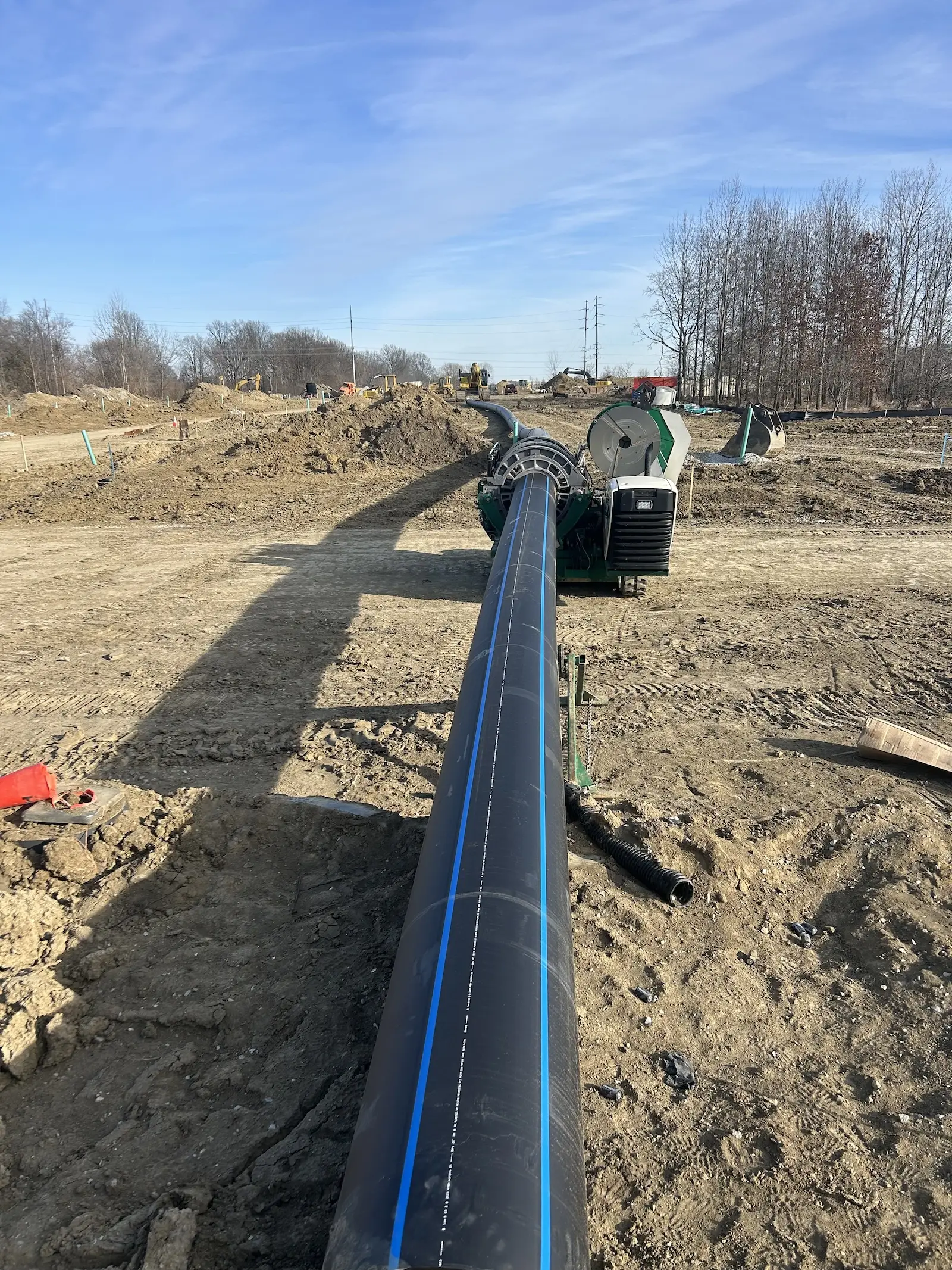 Large black utility pipe with a blue stripe being joined by a fusing machine on a dirt construction site.