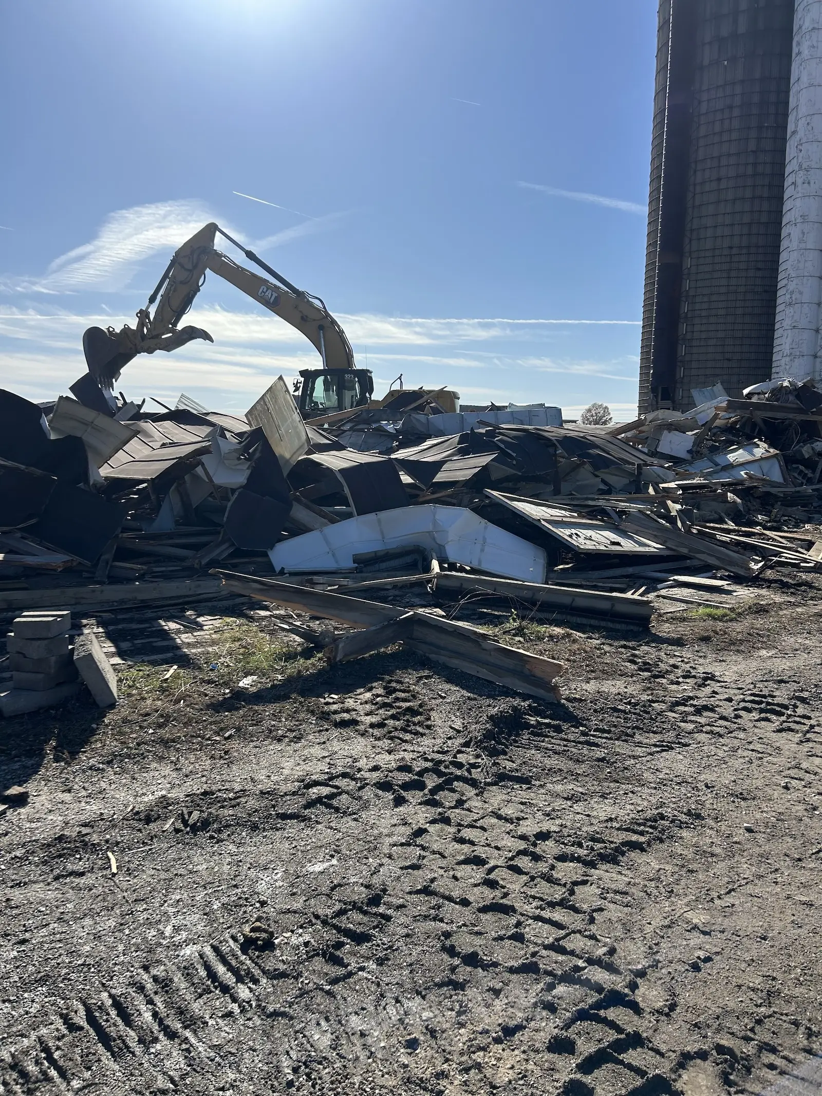 Excavator sifting demolition debris at a construction site with silos in the background.